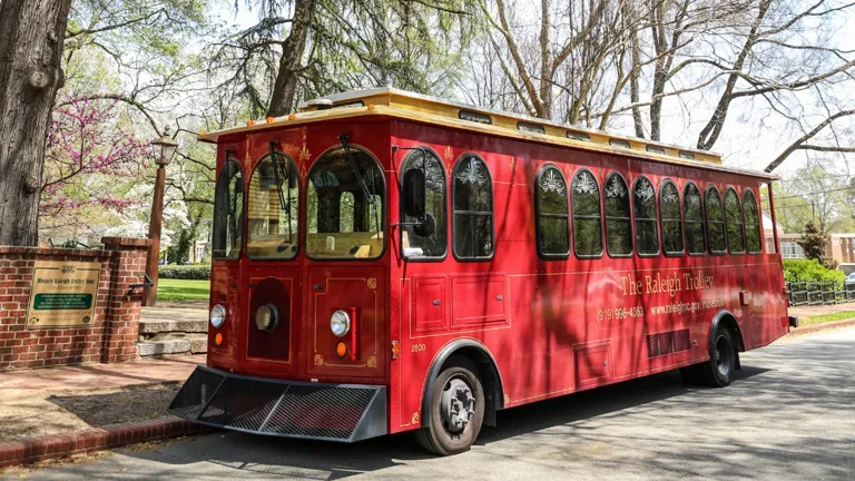 Historic red Raleigh Trolley parked beside a tree-lined street